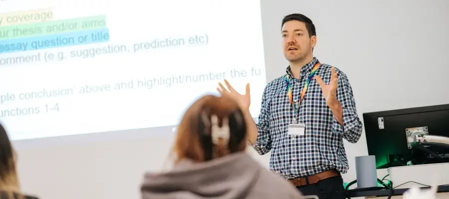 English Language Teacher addressing the class beside the board